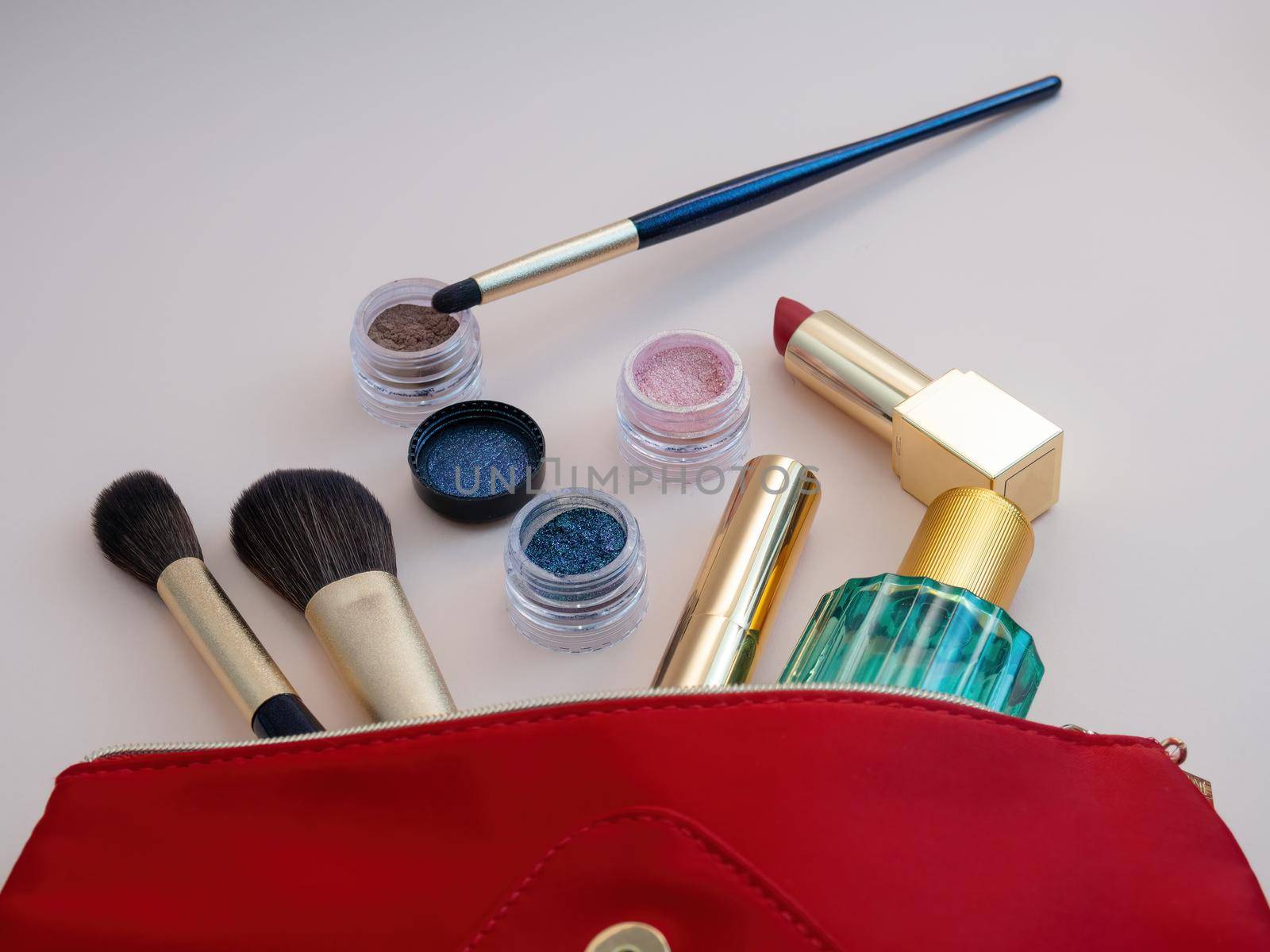 Top view of cosmetics standing out from red cosmetic bag on pink background. Photo