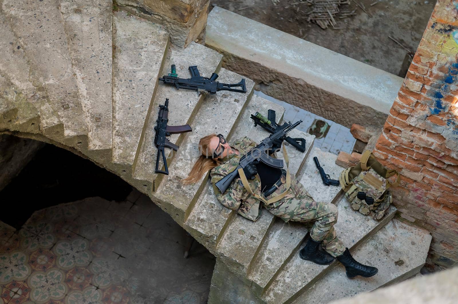 Caucasian woman in military uniform lies on the stairs of an abandoned building and holds a machine gun. View from above. by mrwed54