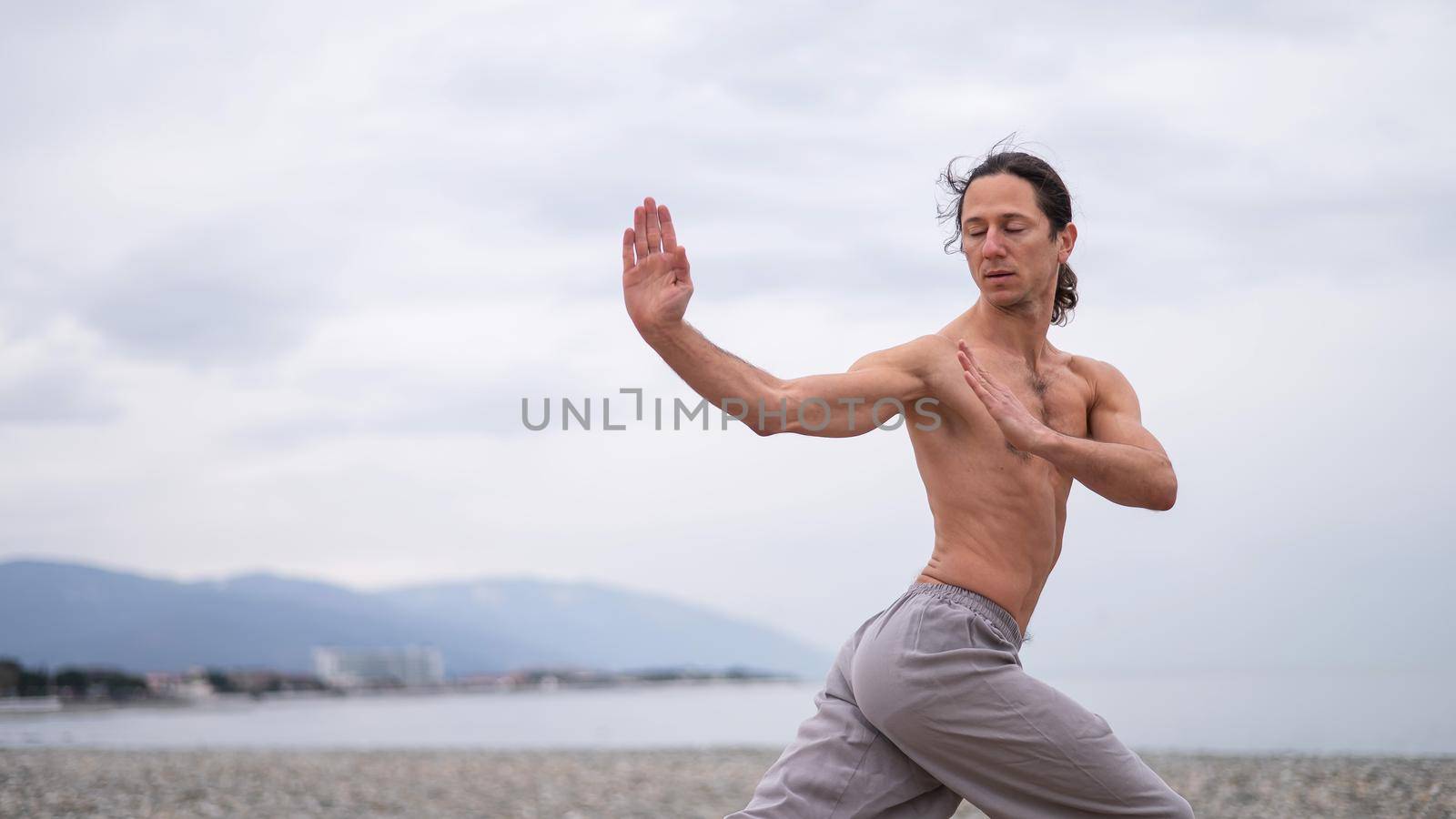 Caucasian man with naked torso practicing wushu on the seashore. by mrwed54