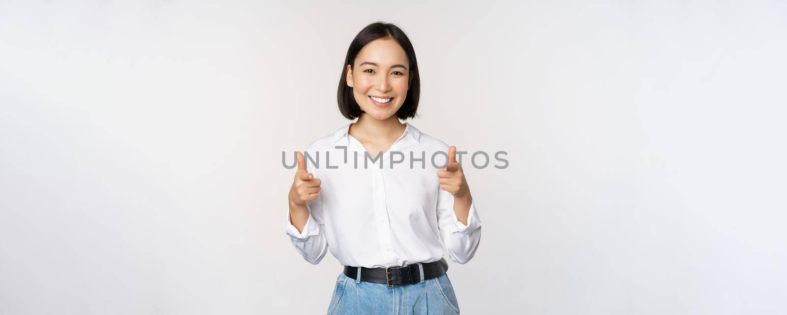 Its you congrats. Smiling attractive asian woman, businesswoman pointing fingers at camera with pleased face, complimenting, inviting you, standing over white background.