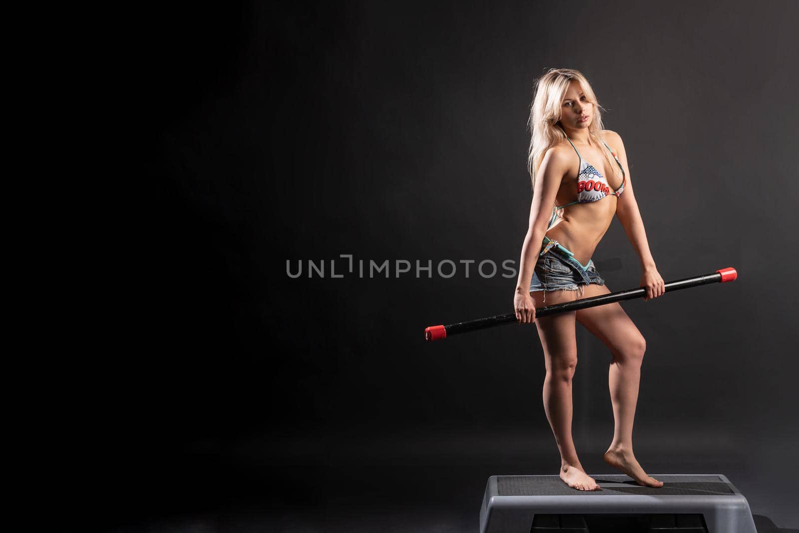 The girl stands on the step platform in a swimsuit on a black background of a beautiful fitness athlete bodybuilder athlete person, girl young fit people, full wellbeing. Happy shape, power club slim attractive