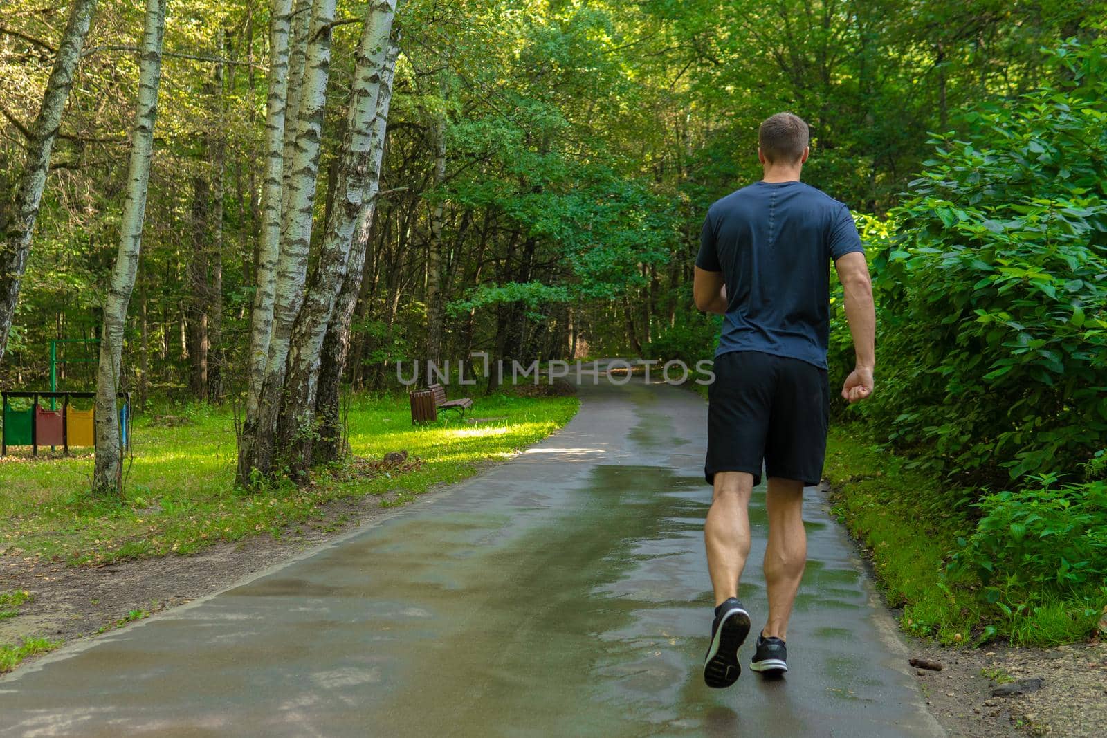 A man athlete runs in the park outdoors, around the forest, oak trees green grass young enduring athletic athlete runner jogger young legs motion, woods running, runners stretches