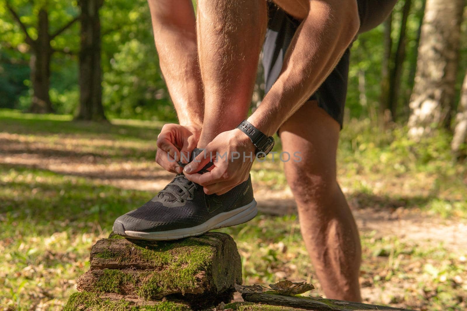 The sportsman is tying the laces of his legs in sneakers close up the athlete runs in the park outdoors, around the forest, oak trees green grass young enduring athletic athlete healthy sport nature, lifestyle outdoor young person jog, outside. body spring, runners stretches