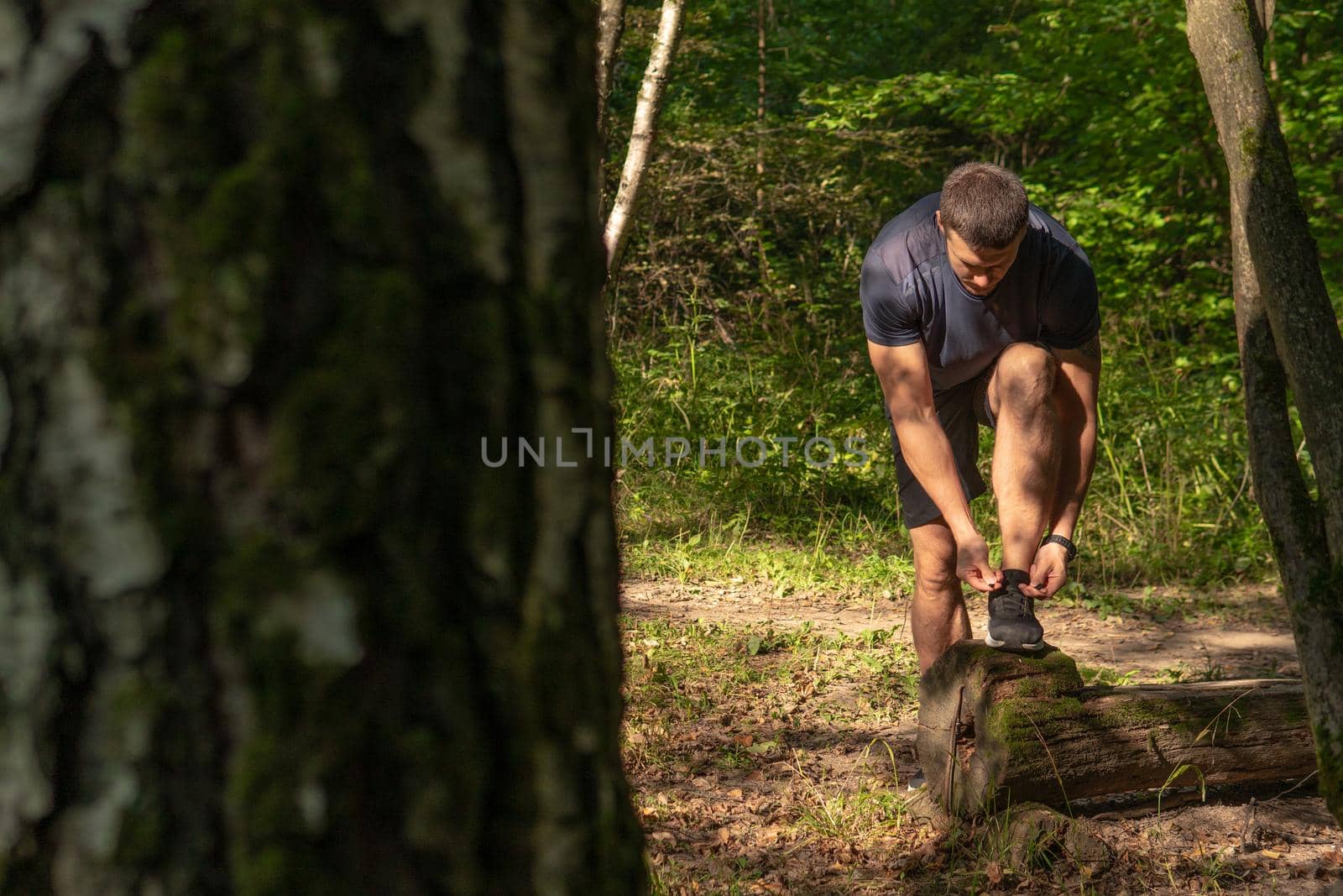 The sportsman is tying the laces of his legs in sneakers close up the athlete runs in the park outdoors, around the forest, oak trees green grass young enduring athletic athlete active athlete nature, fitness trail endurance wellness marathon, woods man. body cross, runners stretches