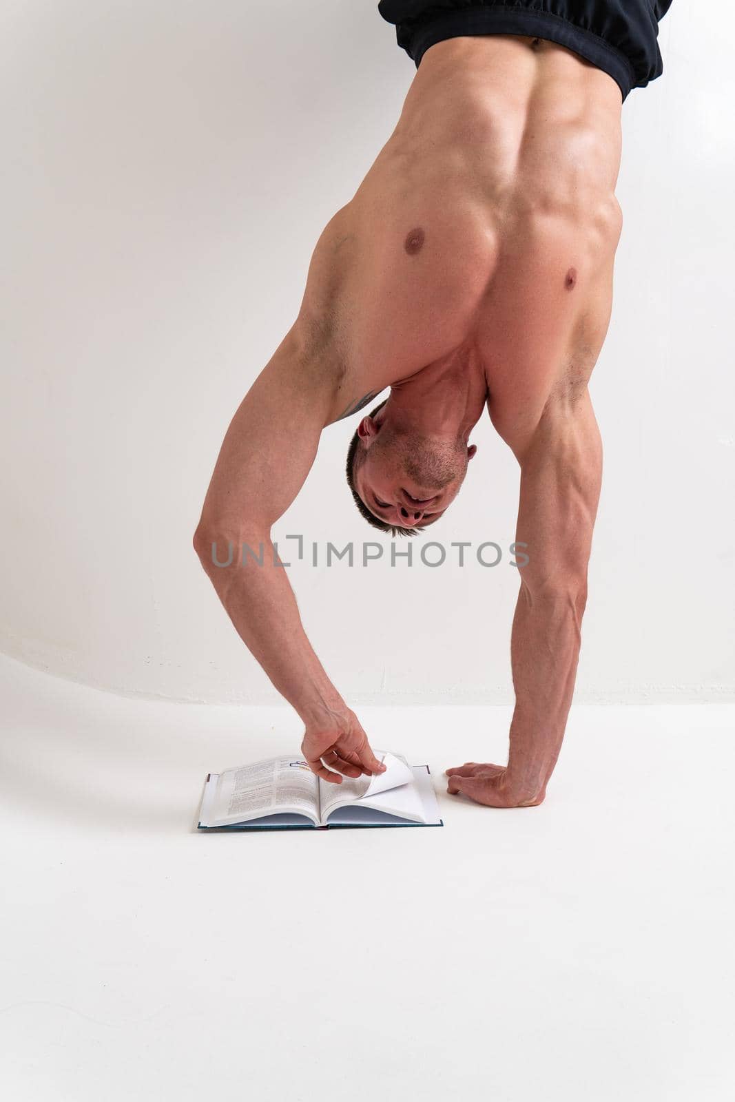 Bodybuilder reads the book on a white background isolated at the bottom of his head on his hands male young athletic fitness bodybuilding guy shirtless, intellectual ABS holding, vision tan