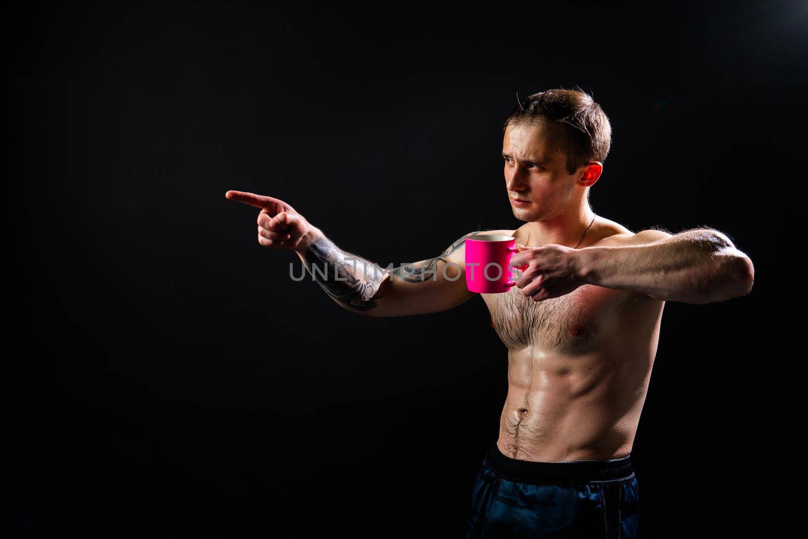 Man on black background keeps dumbbells pumped up in fitness bodybuilding sexy torso, arm weight powerful, person weightlifting. Young power, people fit In the athlete's pink cup he smiles