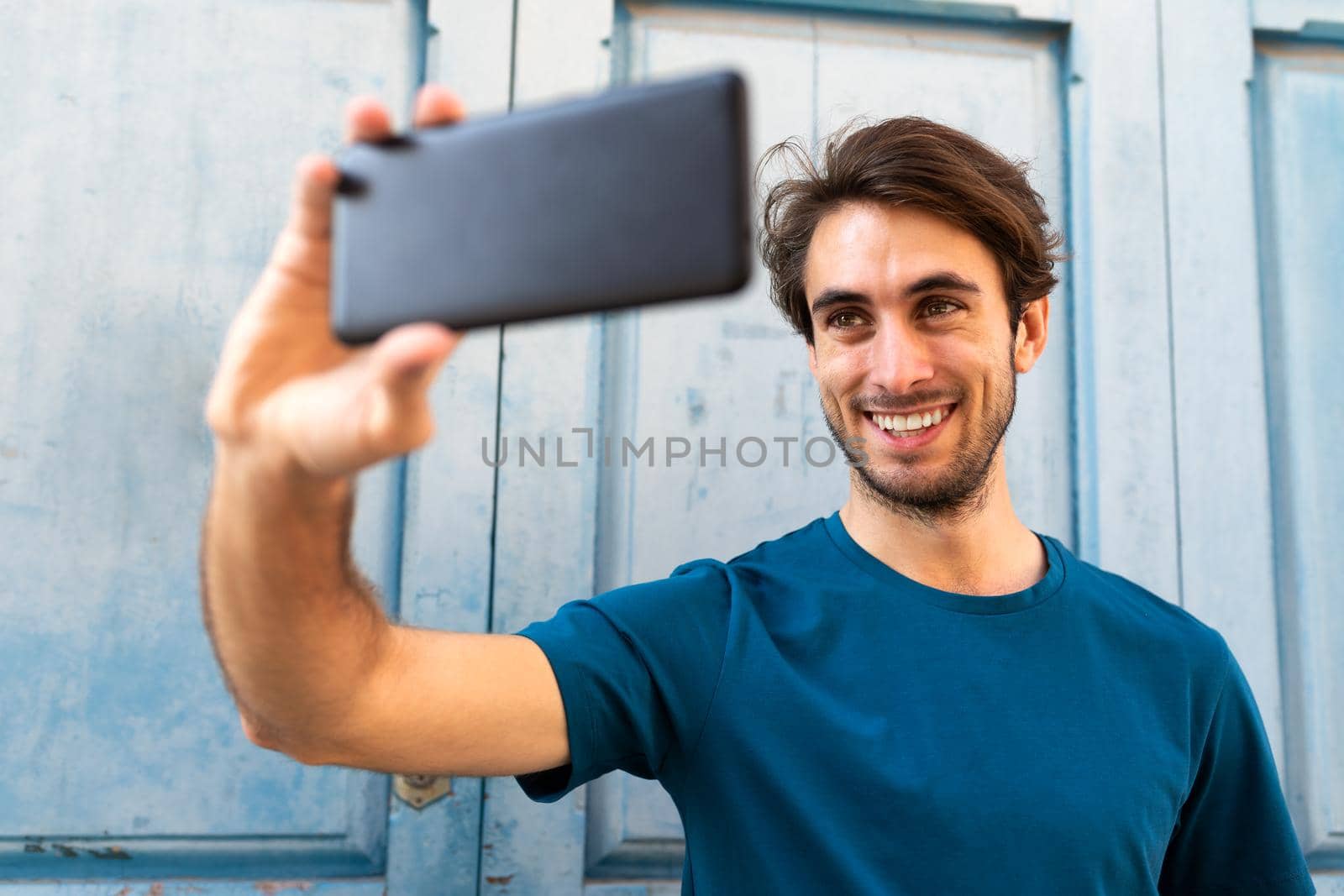 Young caucasian man taking a selfie with smartphone outdoors. Selective focus on face. by Hoverstock