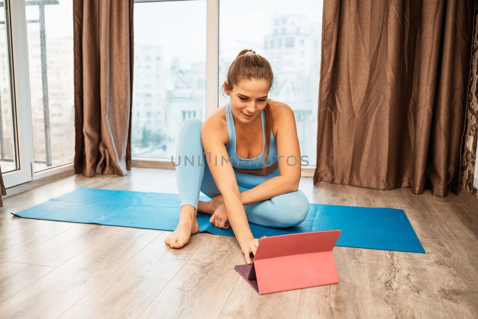 Young athletic attractive woman practicing yoga doing exercises. Works out at home or in a yoga studio, sportswear, blue pants and a full-length top indoors. Healthy lifestyle concept.