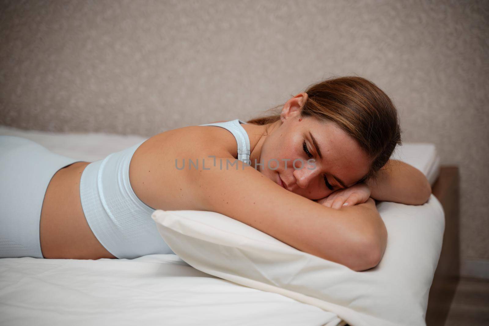 A young woman lies on a bed without a blanket. Bed linen is white