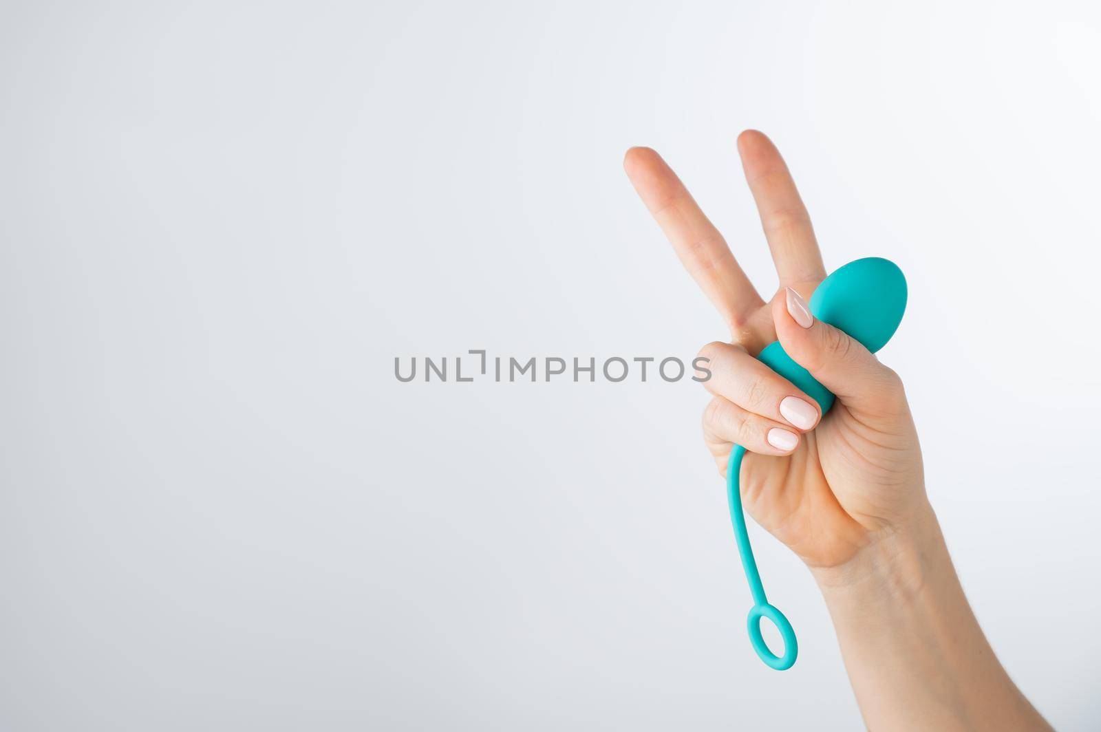 A woman holds a kegel trainer and shows the peace sign. Vaginal eggs on white background.