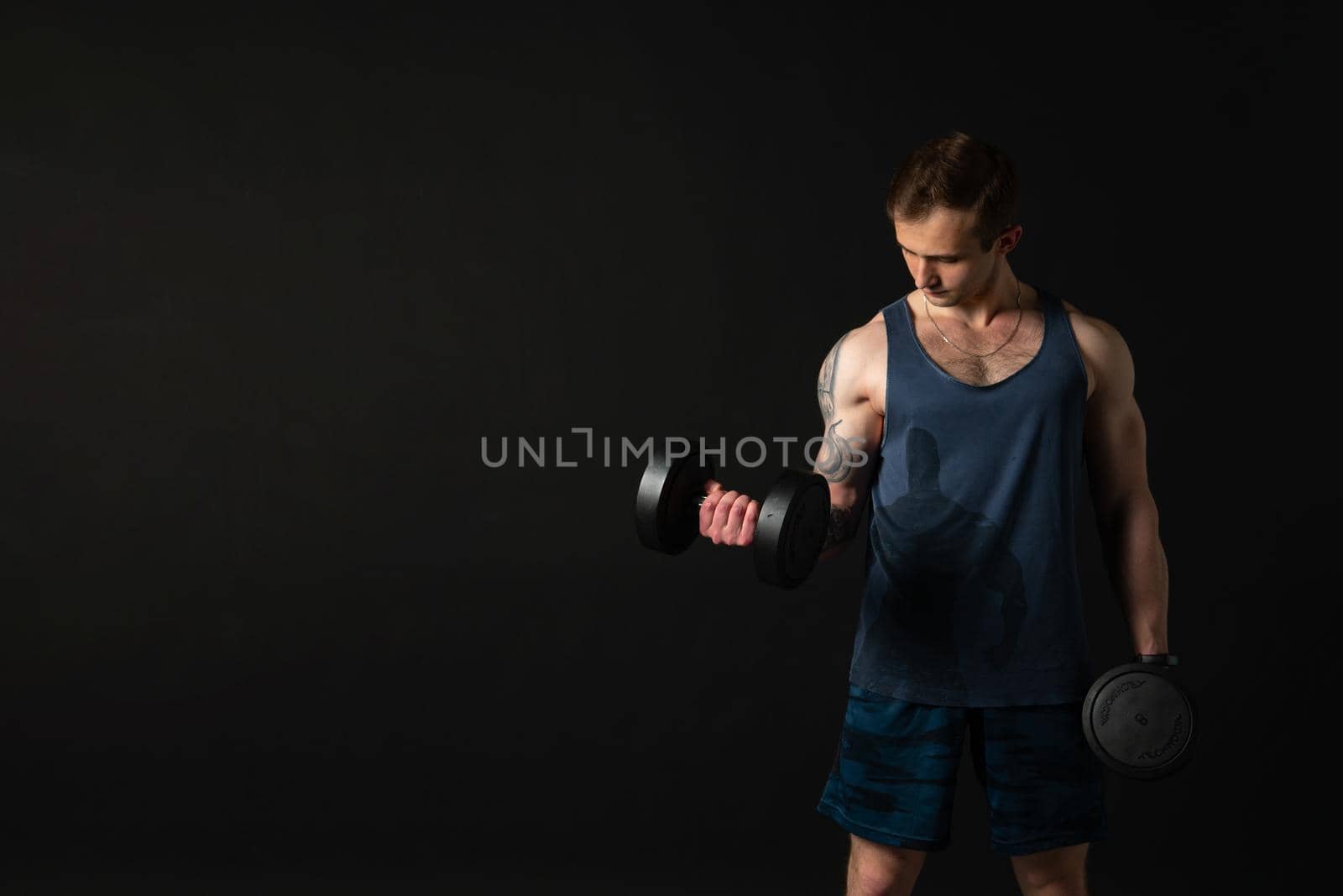 Man on black background keeps dumbbells pumped up in fitness active chest strong hold heavy, shirtless weightlifting. Young handsome people fit