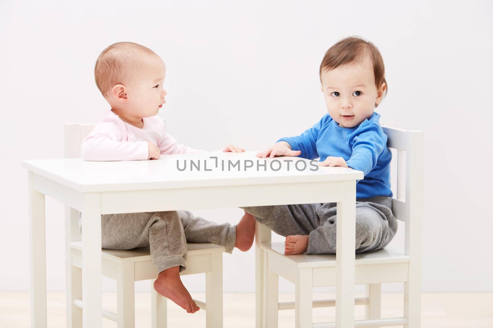 Good times with my new friend. Shot of two adorable little babies sitting together at a table. by YuriArcurs