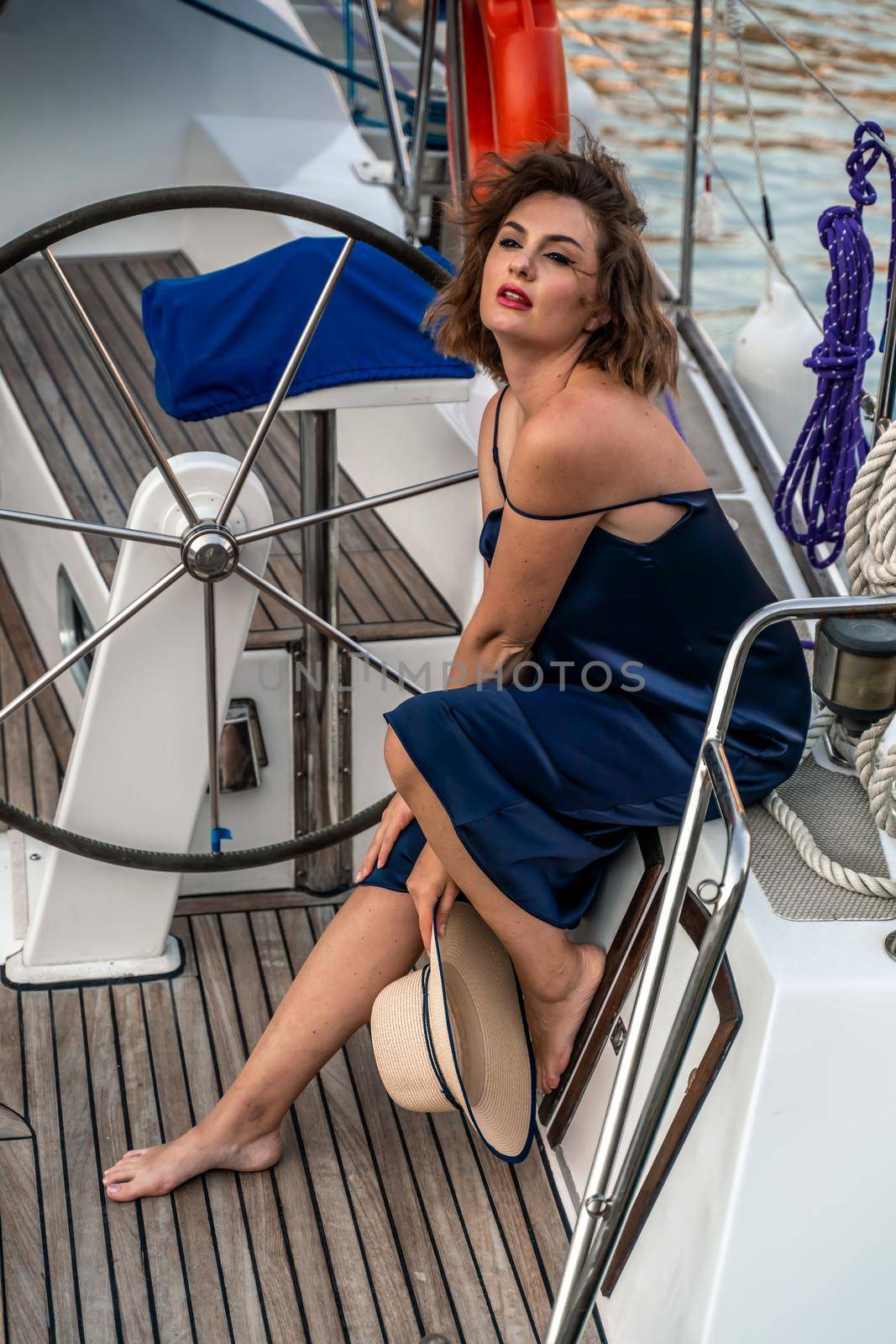 Young happy woman in a blue dress and hat on a yacht. Travel and vacation concept.