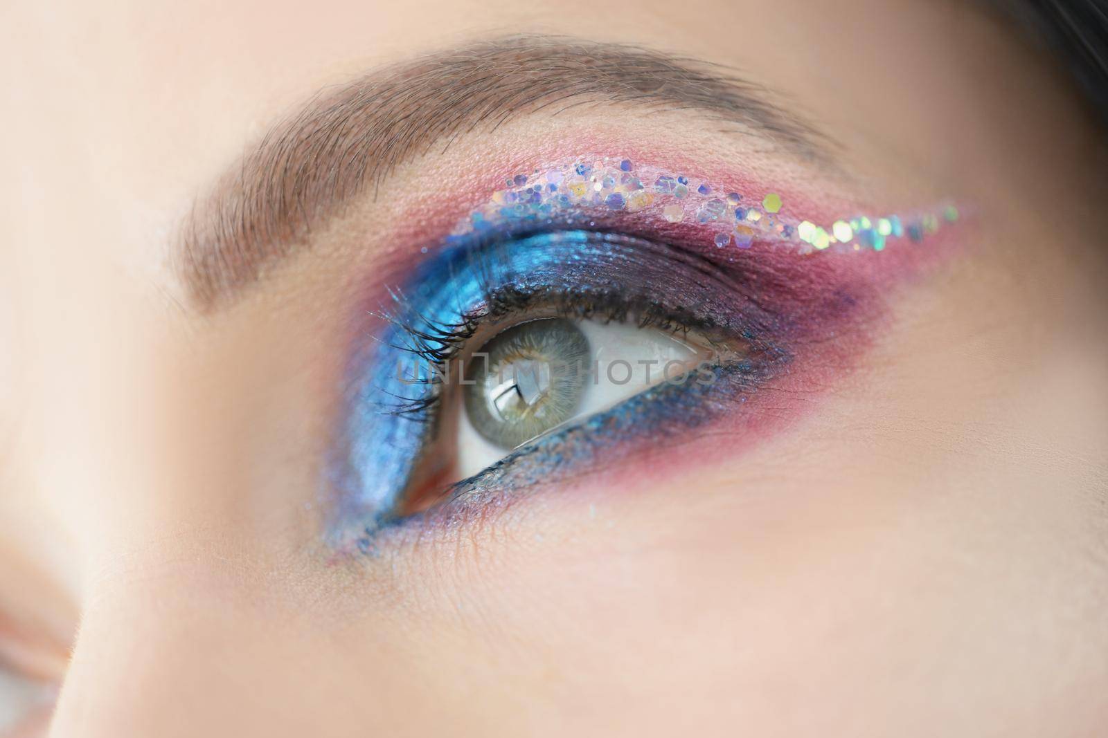 Close-up of colourful glitter and eyeshadows, festive bright eye makeup on girls face. Cat eye technique and colourful mix of shades. Mua, creative concept
