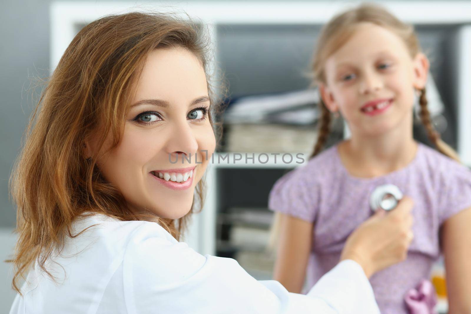 Portrait of smiling pediatrician doctor listen to girl breath and heartbeat with stethoscope. Happy kid on appointment, health. Medicine, childhood concept