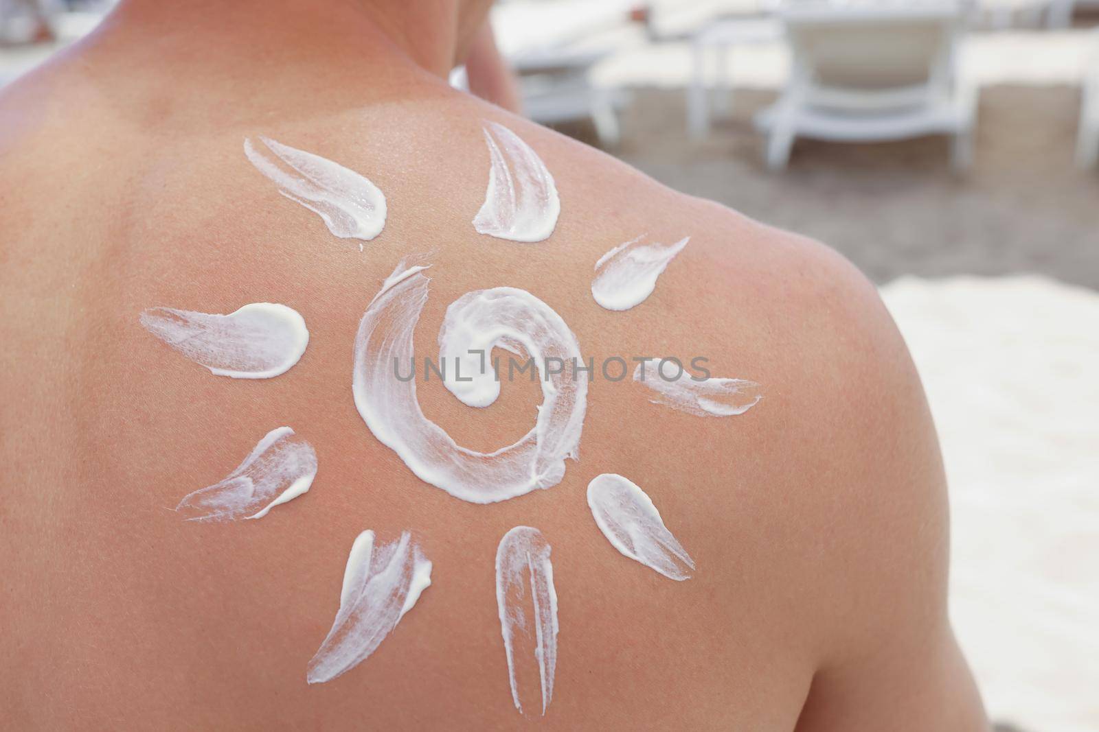 Close-up of persons back with sunscreen picture of sun on it, protect skin from damage. Prepare for sunbathe with spray. Cosmetology, beach, summer concept