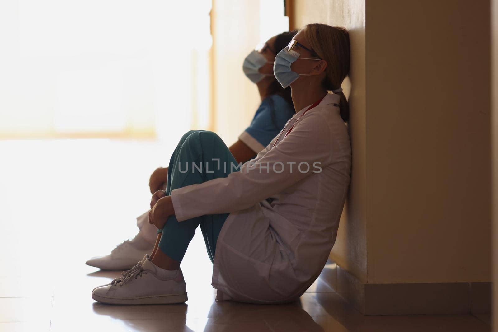 Close-up of exhausted nurses after hard long surgery sitting on floor in hall, difficult shift. Medicine, save life, healthcare, clinic, help concept