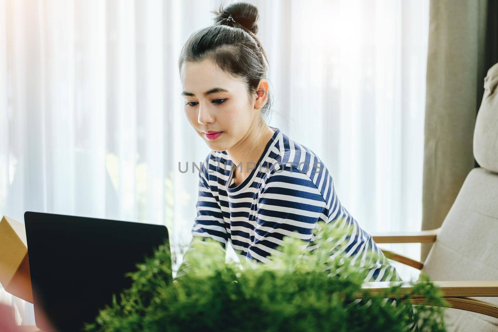 Online merchandising business idea, beautiful girl holding a parcel delivery box and using a computer to input Track And Trace parcel numbers to customers. by Manastrong