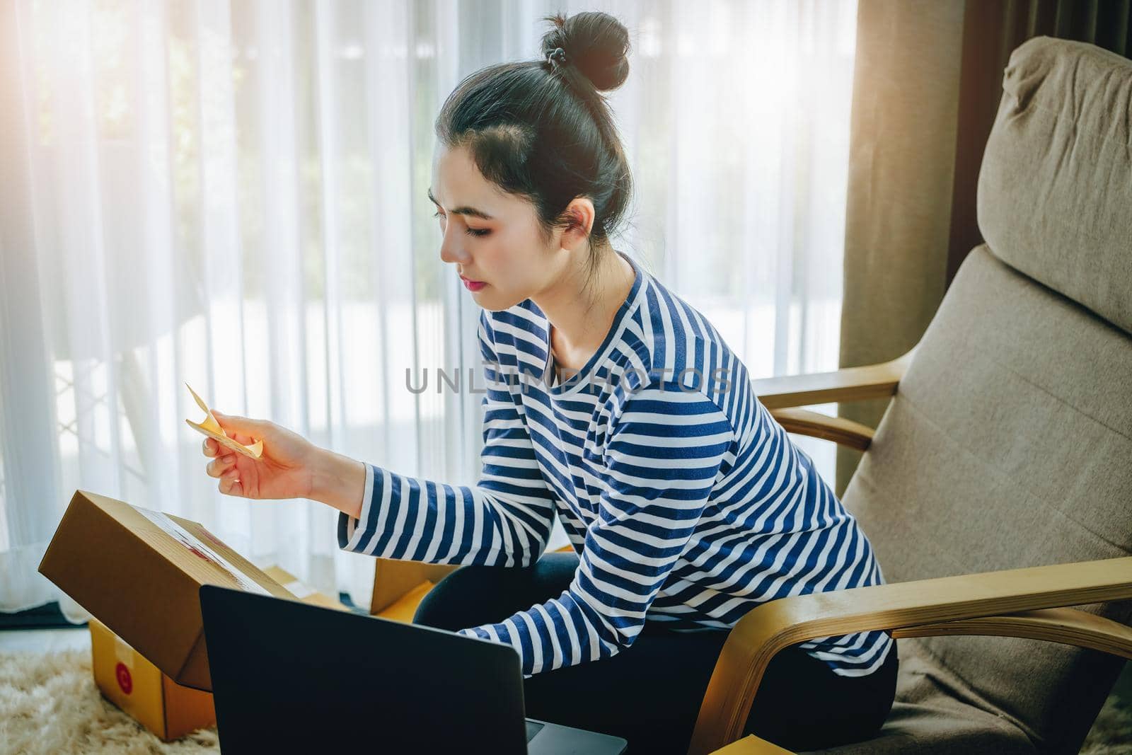 Online merchandising business idea, beautiful girl holding a parcel delivery box and using a computer to input Track And Trace parcel numbers to customers. by Manastrong