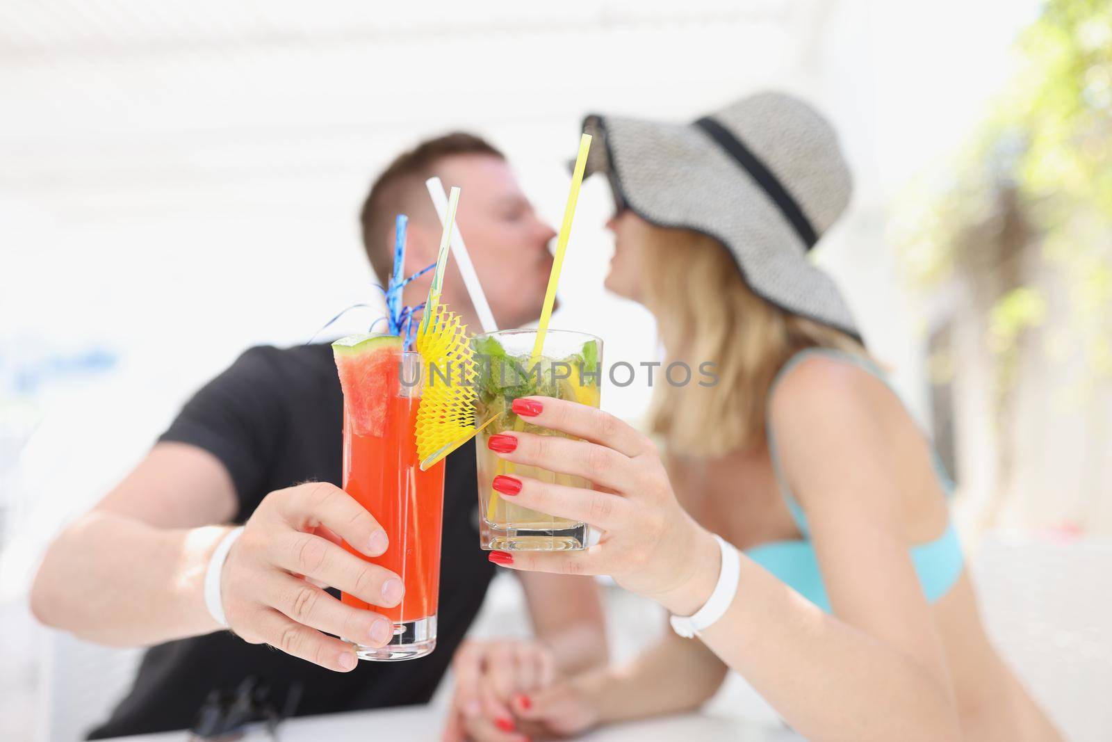 Portrait of woman and man kissing and having cooling cocktails, couple resting on luxury resort, chill, swimming pool. Vacation, toast, holiday concept