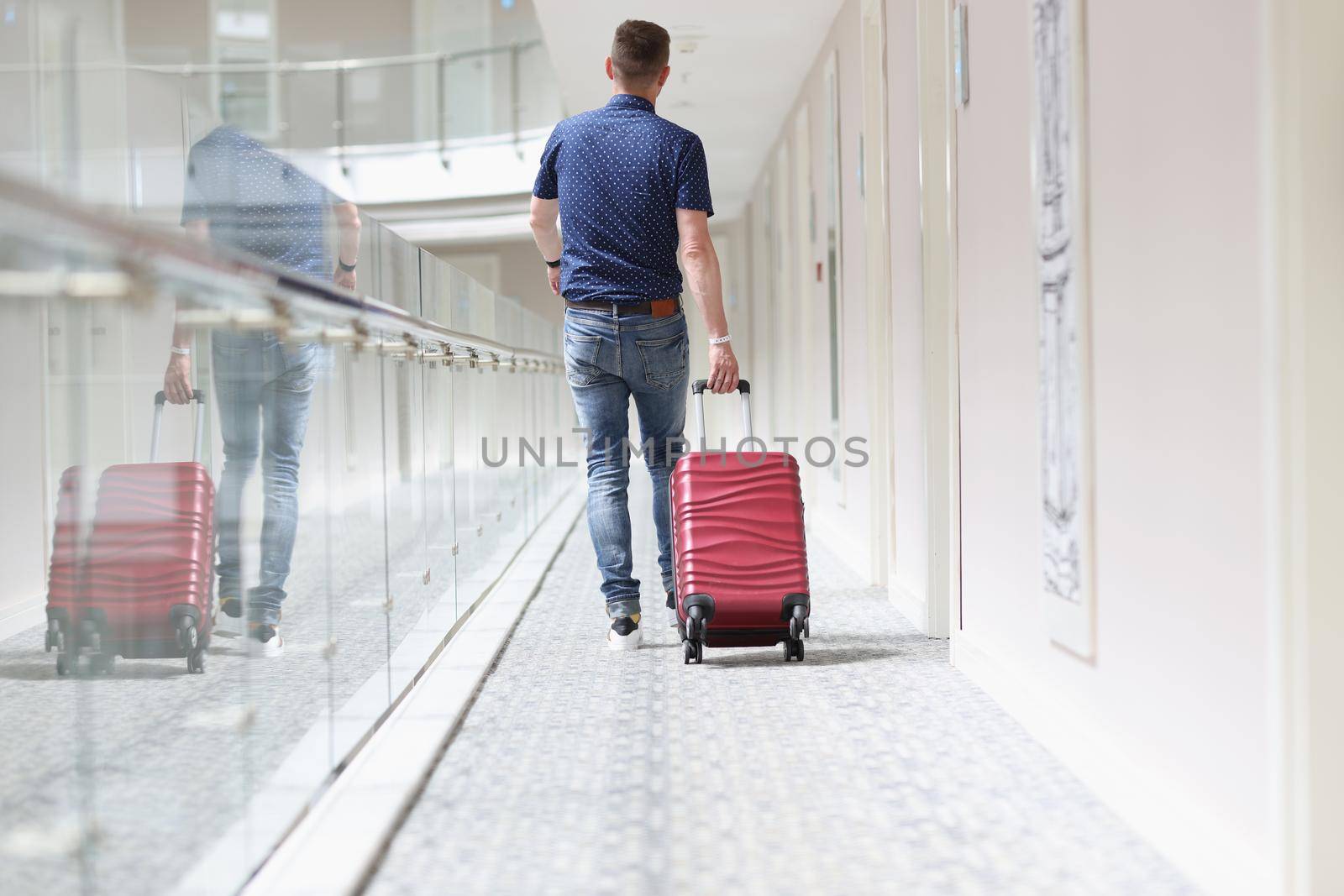 Low angle of young male pulling red luggage behind, search for his room in hotel building. Traveling, adventure, voyage, journey, tourism, resort concept