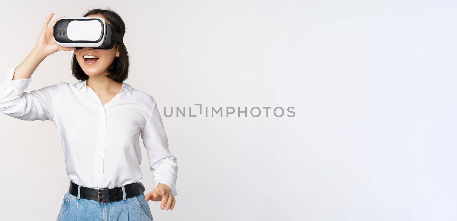 Excited young woman enter virtual reality in her glasses. Asian girl using vr headset, standing over white background.
