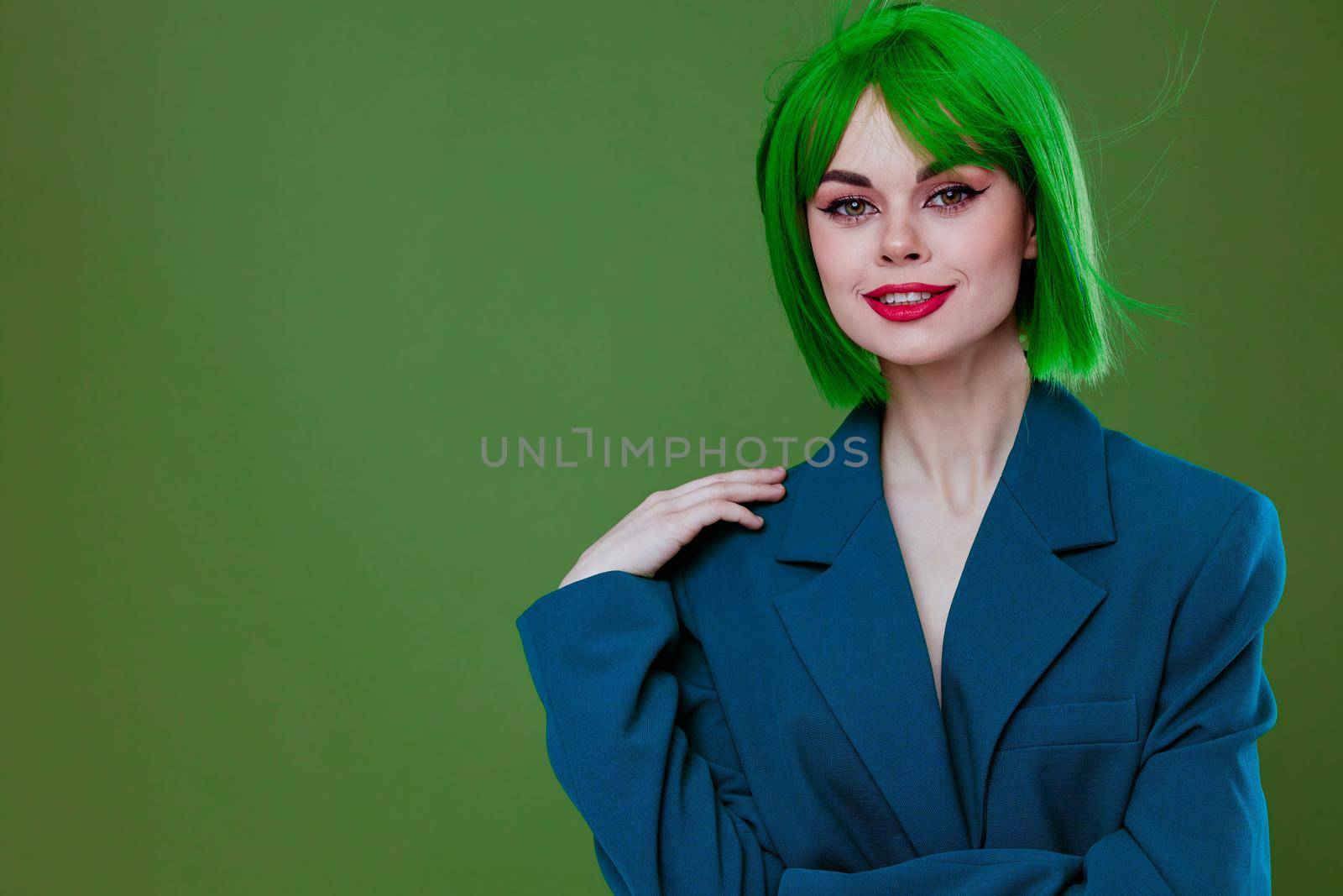 Positive young woman wearing a green wig blue jacket posing green background unaltered by SHOTPRIME