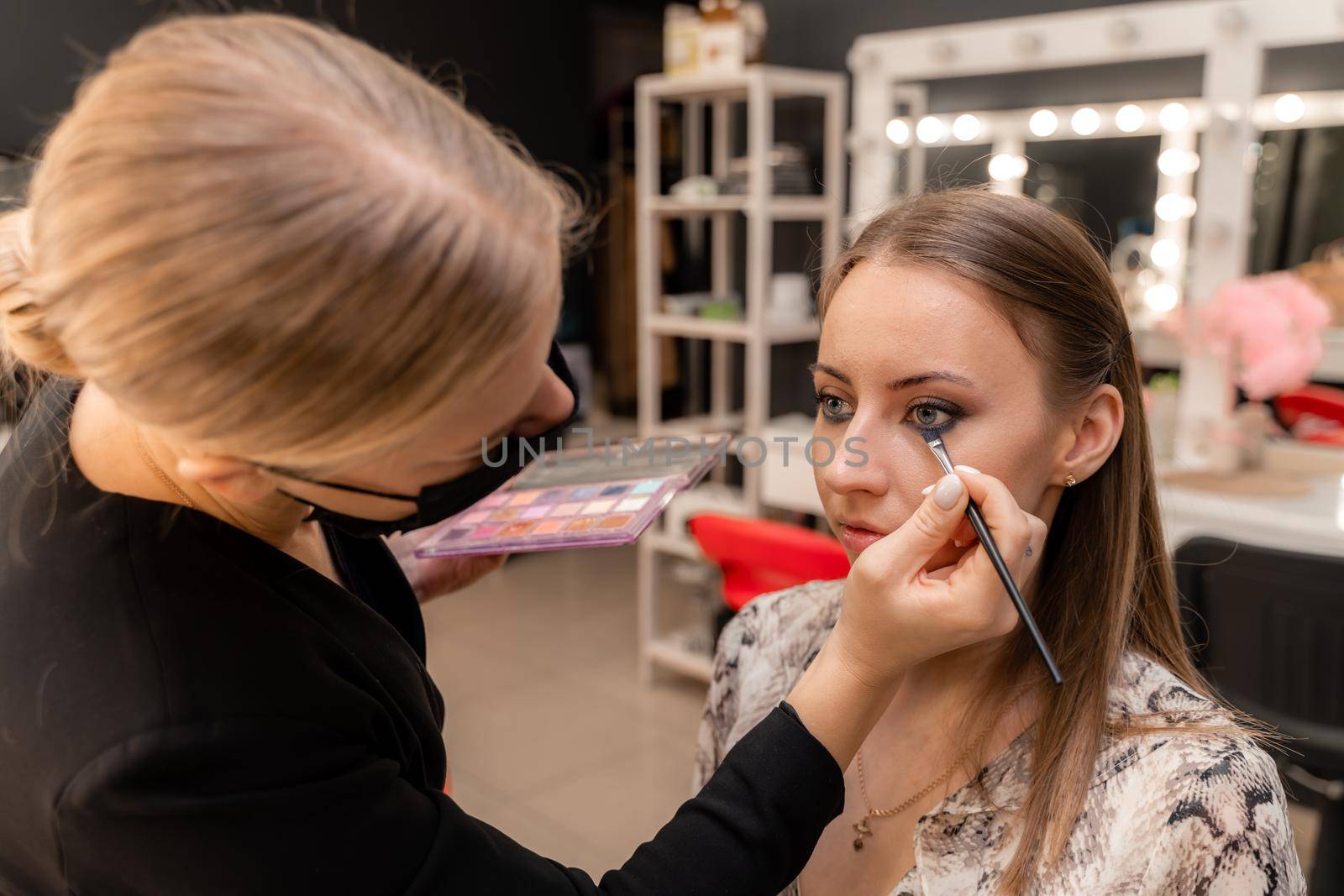 Make-up artist working with brush on model eyes Close up of applying make up on young girl,semi profile, professional make up in beauty studio.