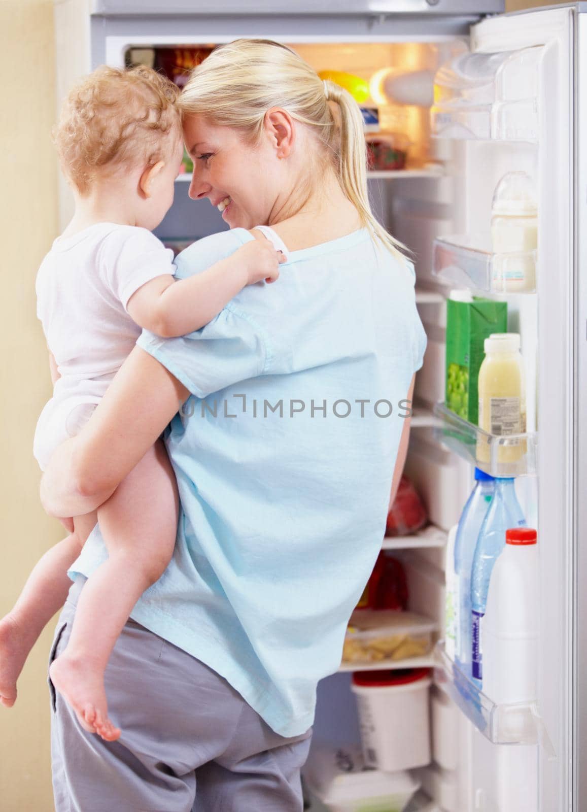 A mother standing in front of the fridge and holding her baby in her arms.
