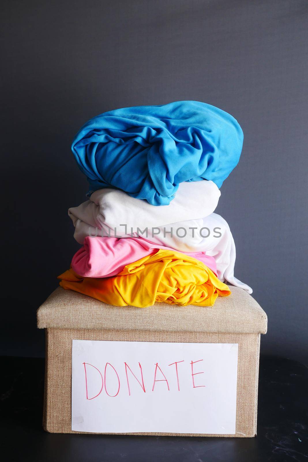 Donation box with stack of clothes against black background .