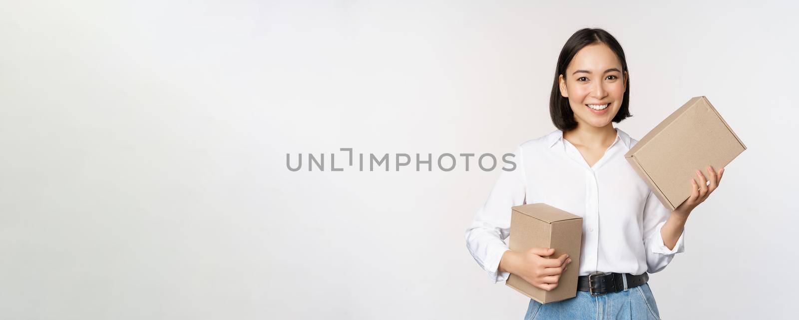 Concept of shopping and delivery. Young happy asian woman posing with boxes and smiling, standing over white background.