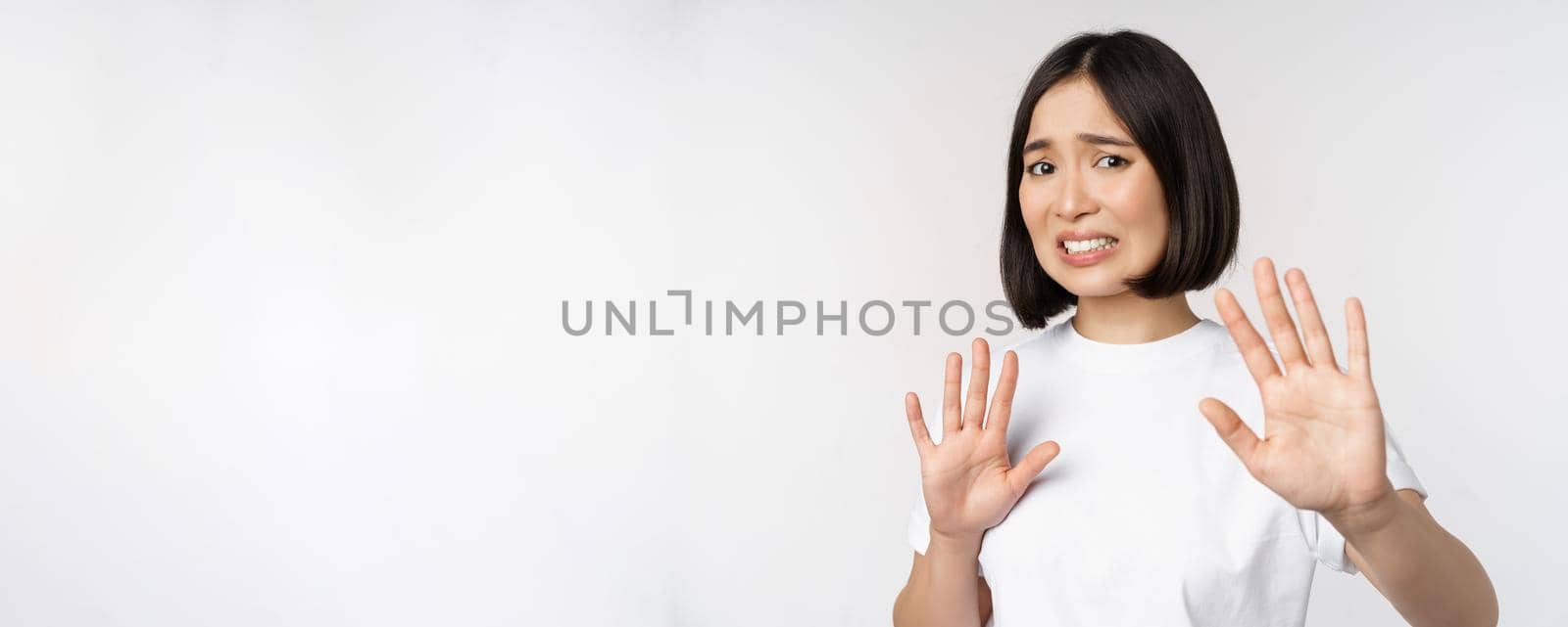 Disgusted asian woman rejecting smth, grimacing from dislike and aversion, stare with cringe, refusing offer, standing over white background.