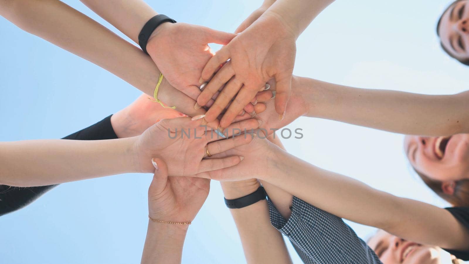Cheerful girls join hands together as a sign of unity and joint successful work. Teamwork stacking hand concept. by DovidPro