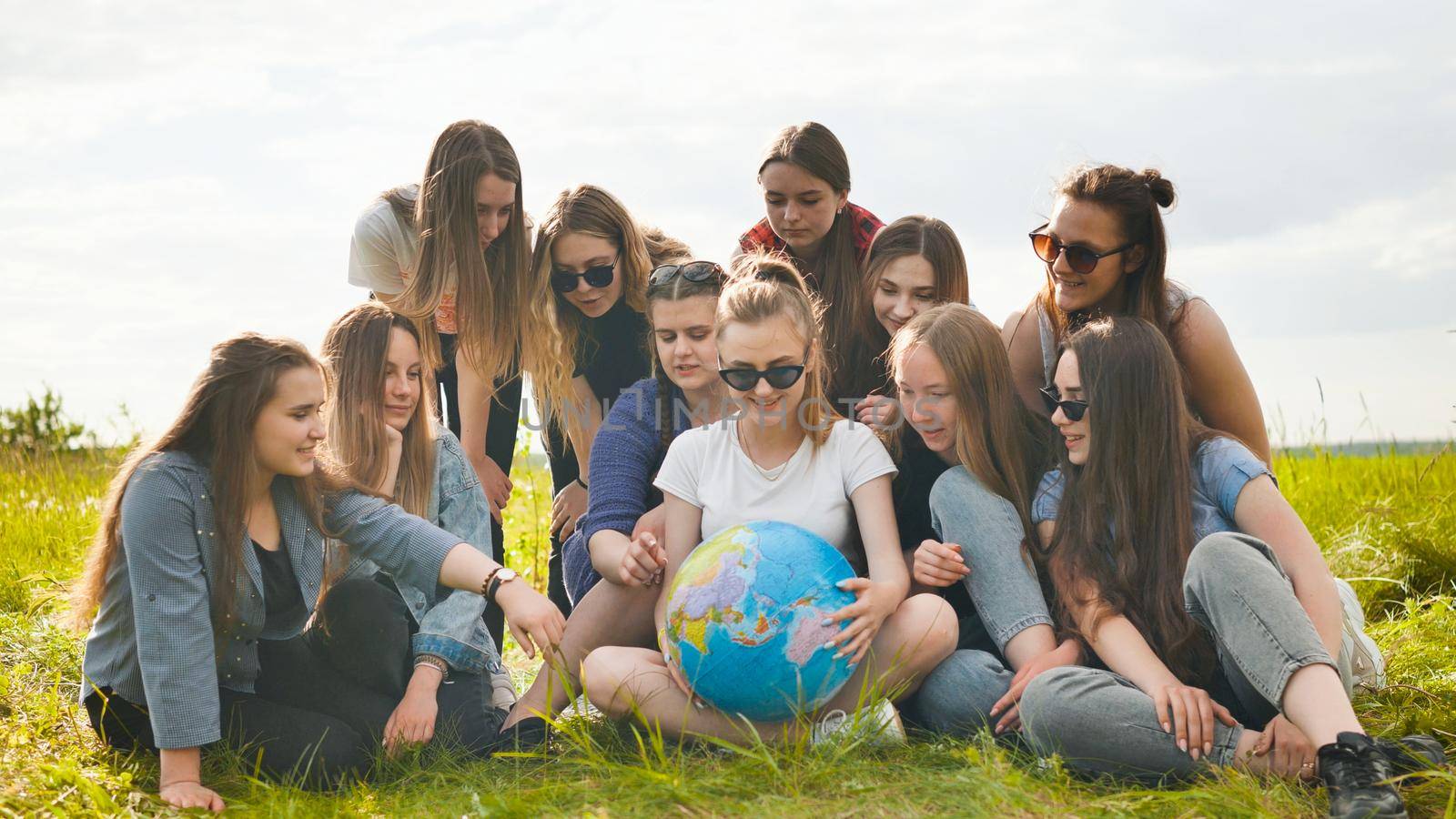 A group of cheerful girls is exploring the globe of the world in the meadow. by DovidPro