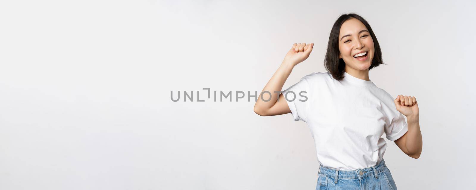 Happy dancing korean girl posing against white background, wearing tshirt by Benzoix