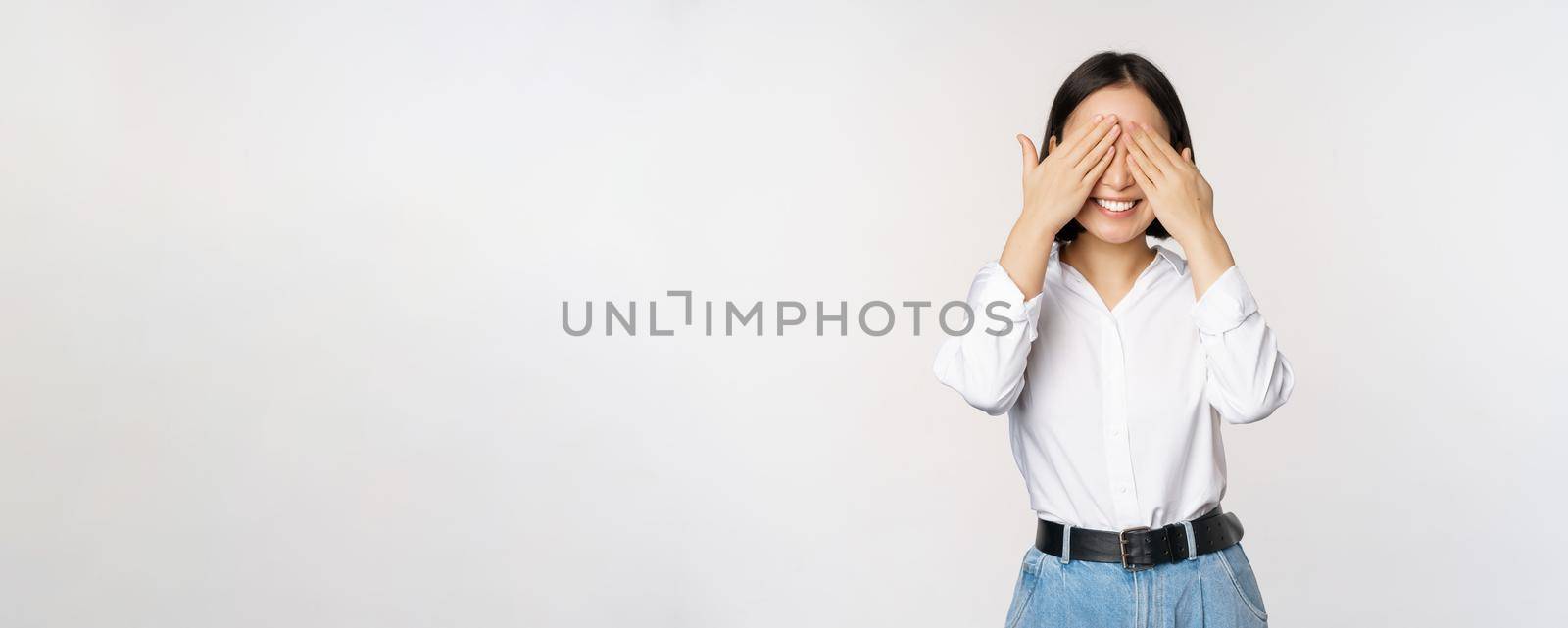 Image of young asian woman close her eyes and smiles, waits for surprise, anticipates, stands over white background by Benzoix