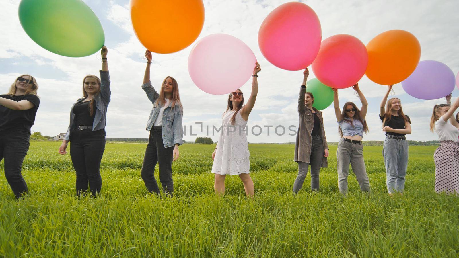 Girls friends are walking across the field with large balloons and colorful balloons