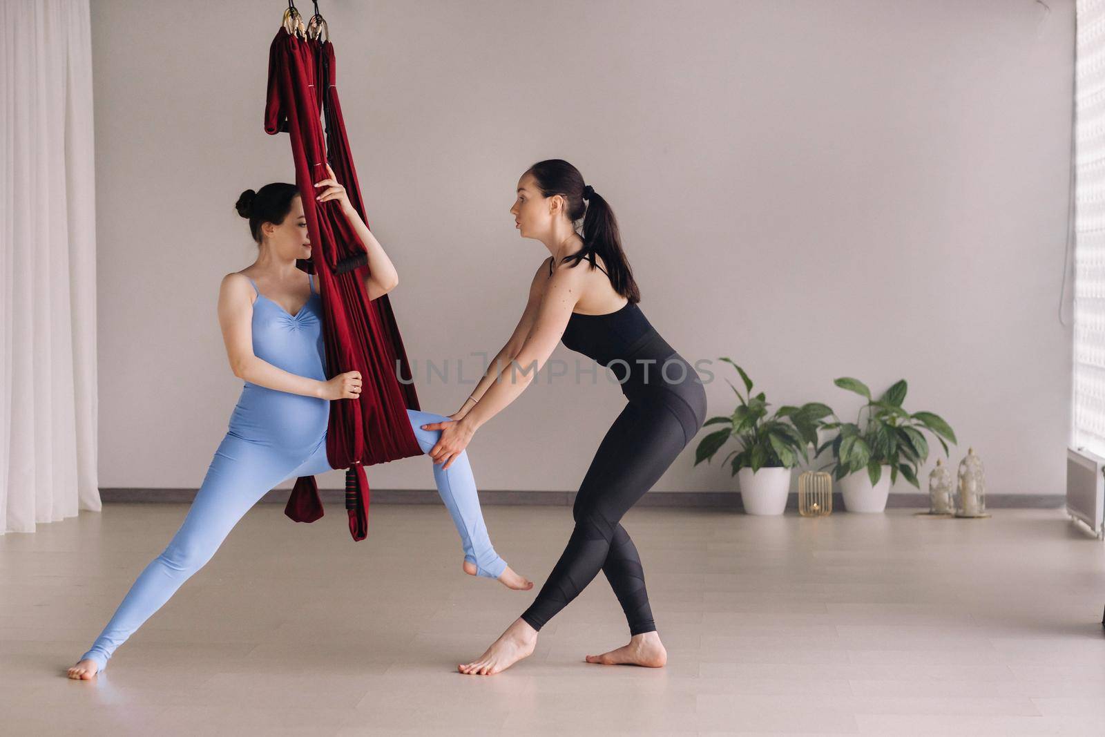 Pregnant girl. A woman with a trainer does yoga in a hammock in the gym. The concept of a healthy lifestyle, motherhood.