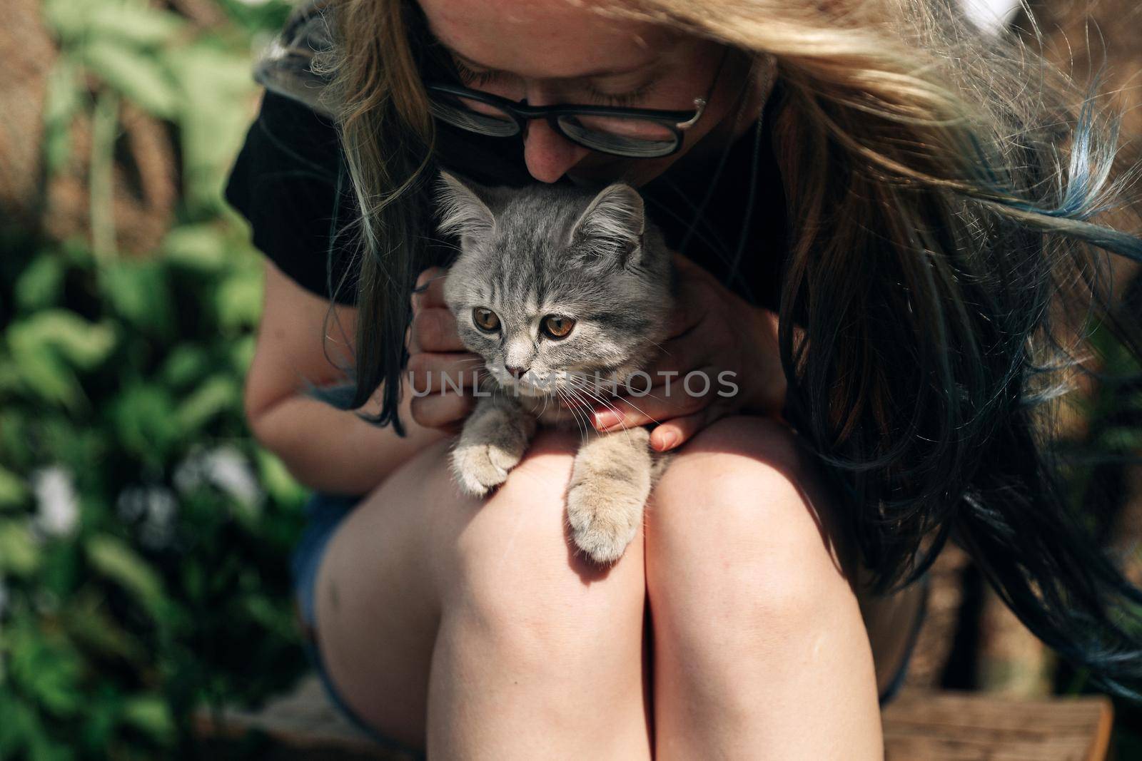 A young woman is holding a Scottish Straight kitten outdoors. Close-up, natural daylight