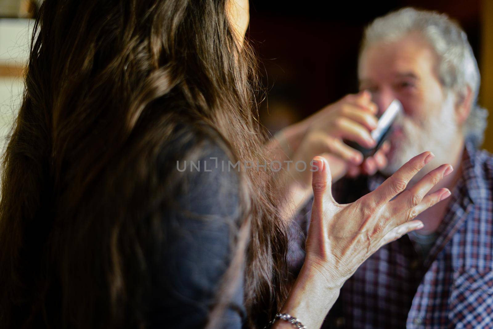 caucasian man drinking wine and getting drunk at home stressing younger hispanic woman wife - alcoholism and domestic violence concept by verbano