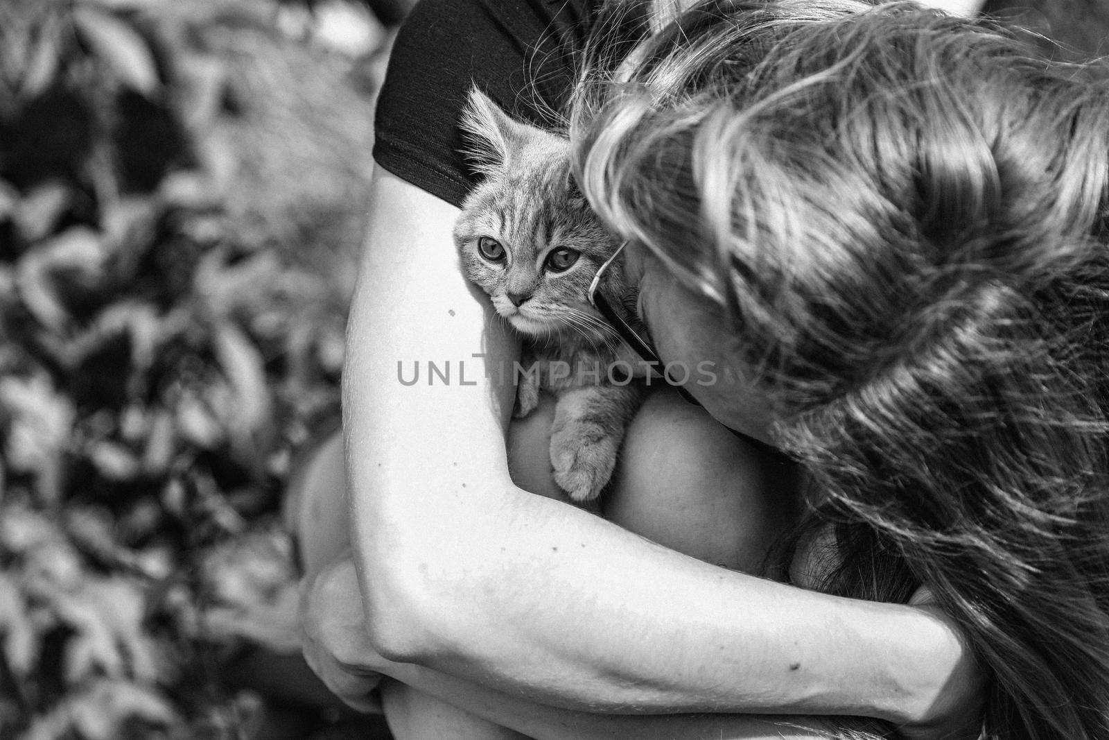 Young woman hugging a kitten of the Scottish Straight breed. Black and white photo close up outside. High quality photo