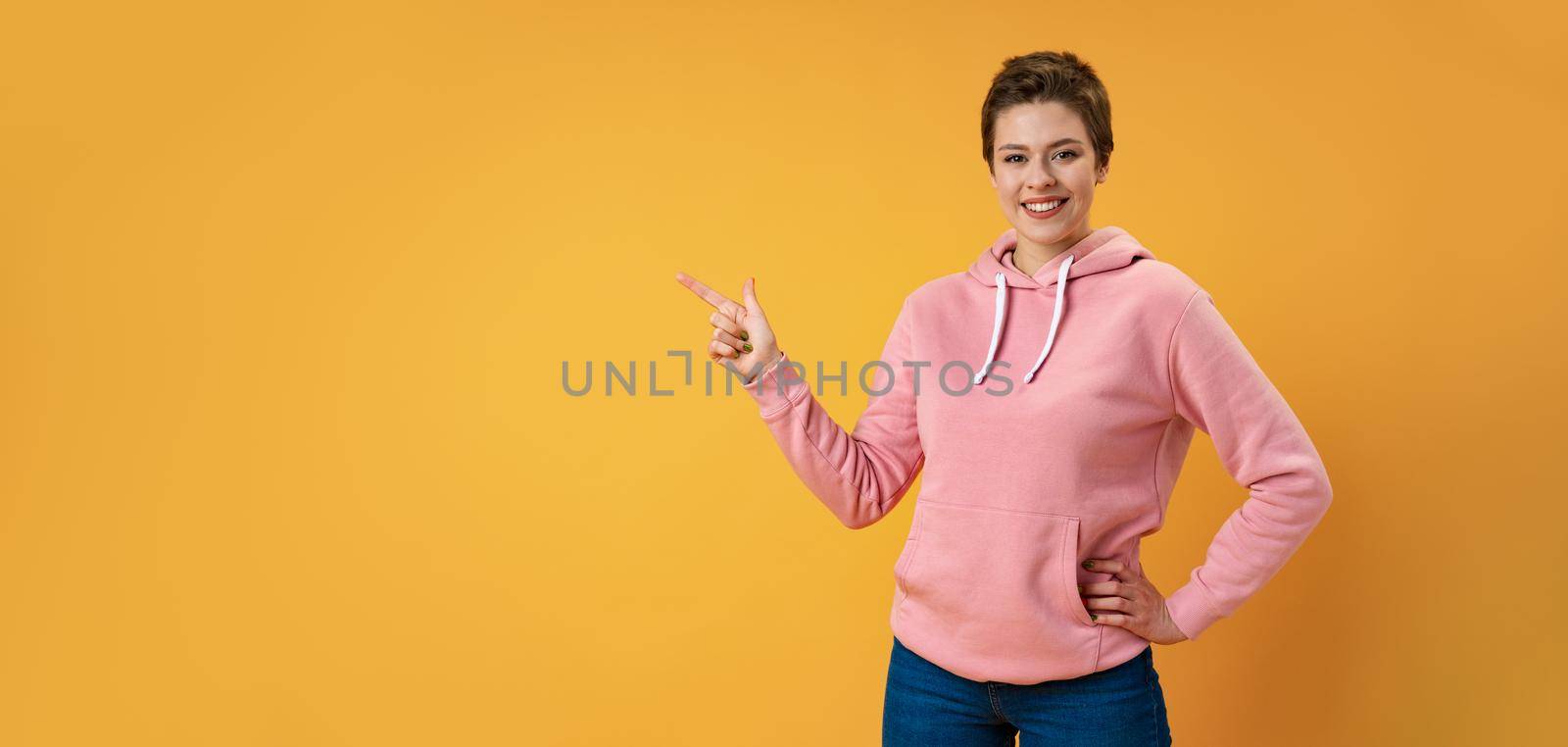 Young woman with short hair over studio color background pointing finger to the side, close up