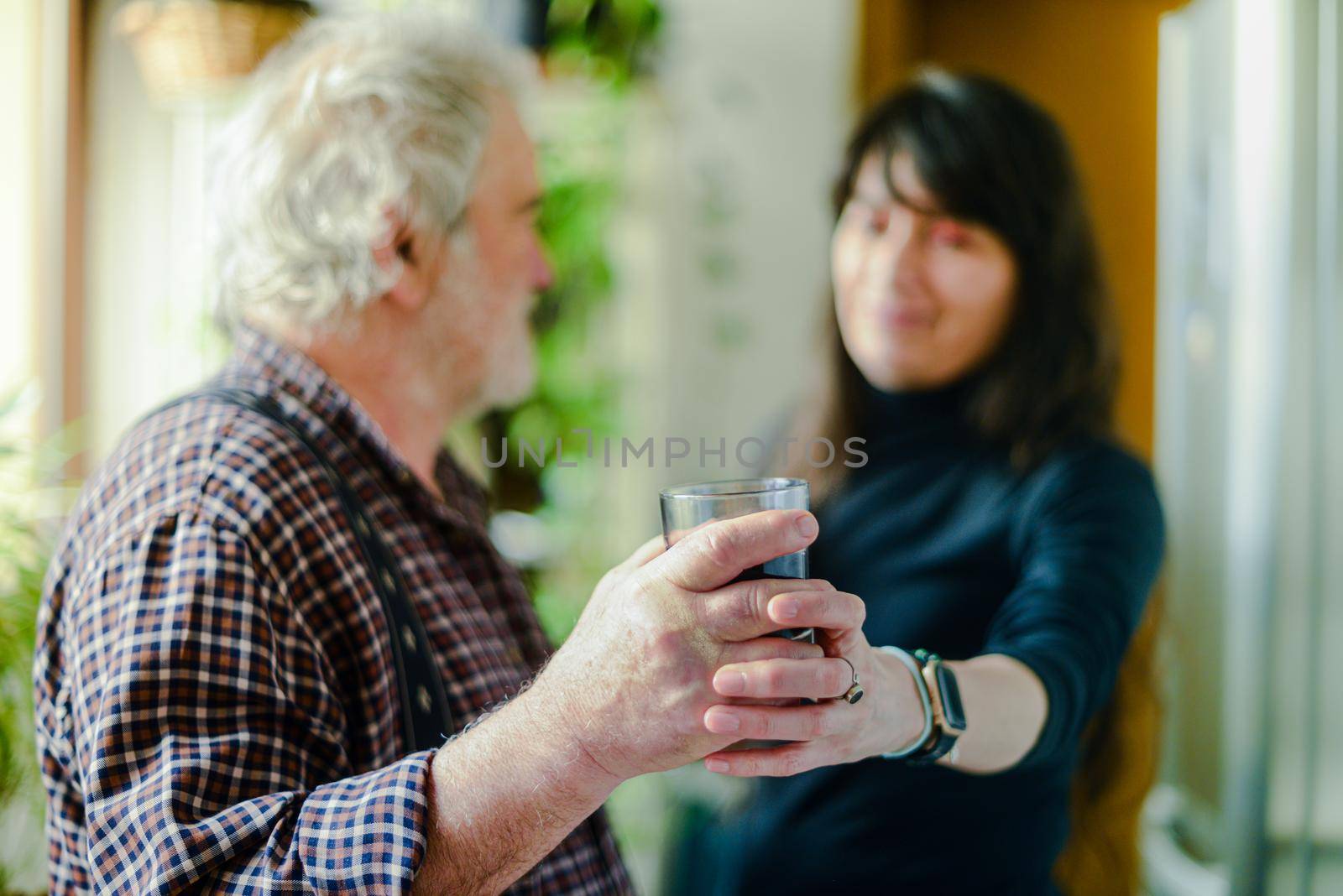 caucasian man drinking red wine and getting drunk at home stressing younger hispanic womancaregiver adn wife - alcoholism and domestic violence concept. High quality photo