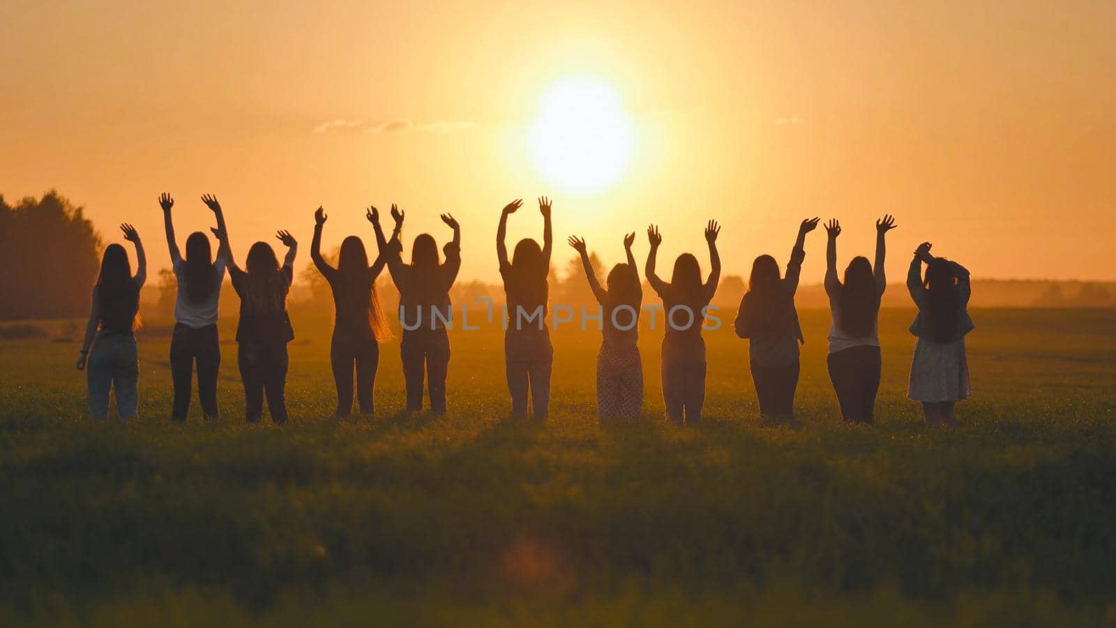 Silhouette of friends of 11 girls waving their hands at sunset in the field