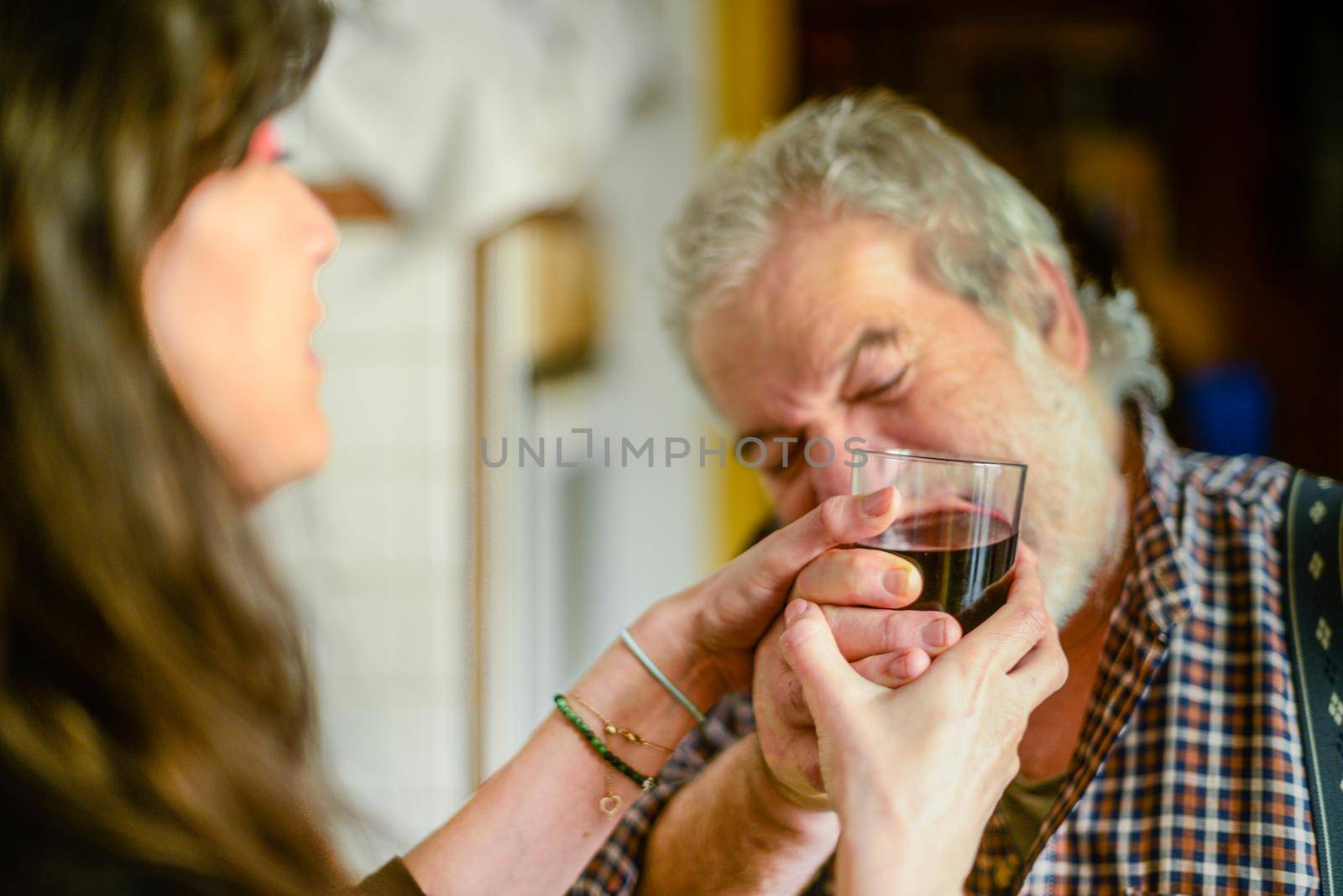 caucasian man drinking red wine and getting drunk at home stressing younger hispanic womancaregiver adn wife - alcoholism and domestic violence concept. High quality photo