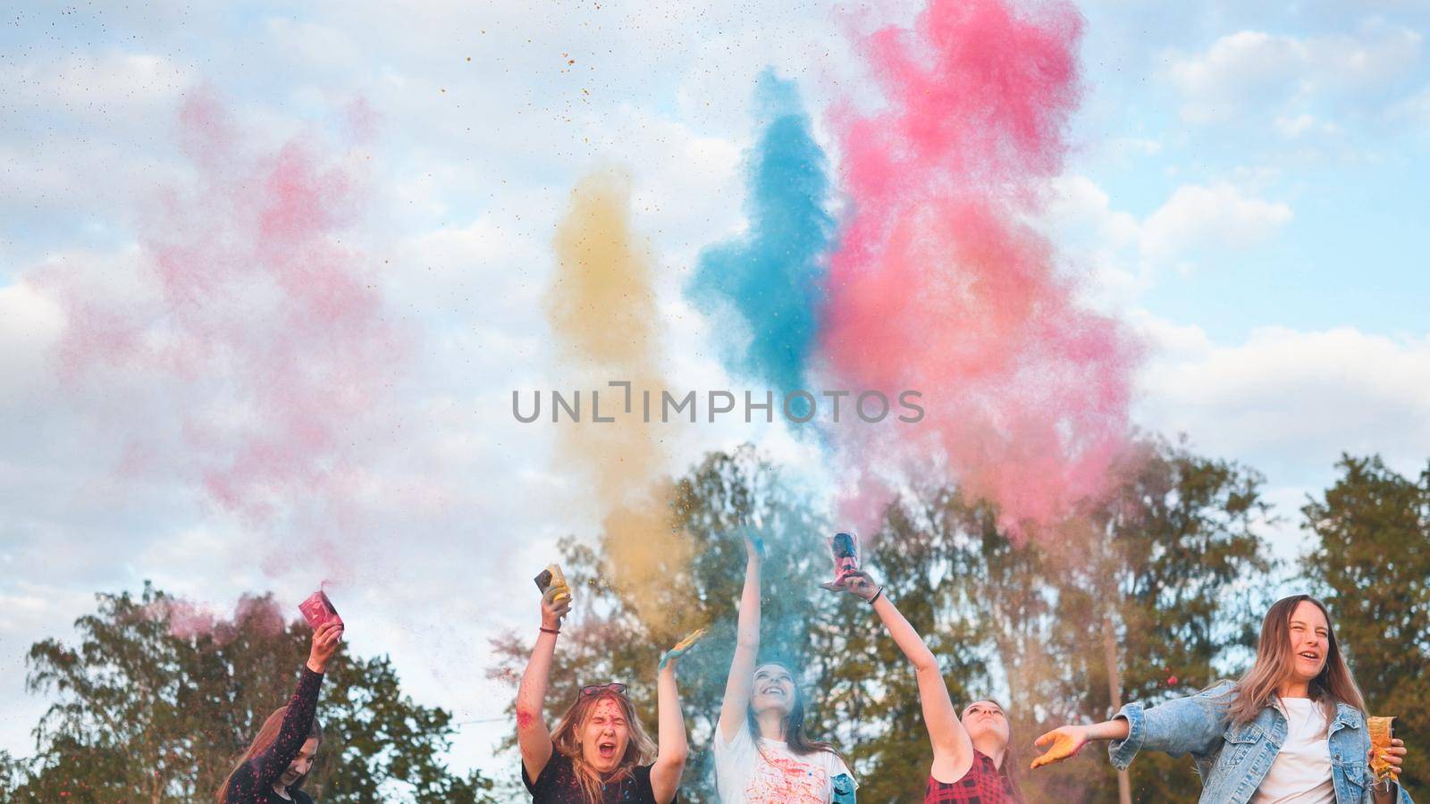 Cheerful girls toss up multi-colored powder. Holi holiday