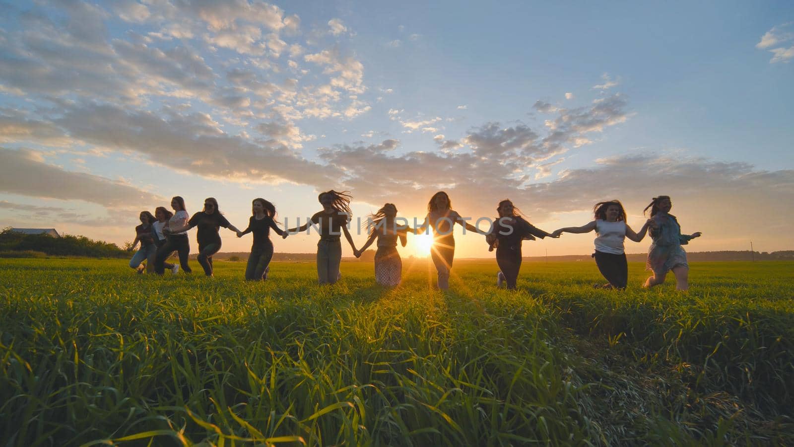 Eleven cheerful girls run to the meeting across the field in the summer, holding hands