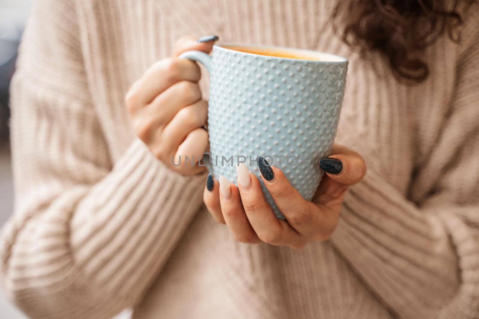 A girl in a beige sweater with a blue mug in her hands. Blue porcelain mug mockup for your design.