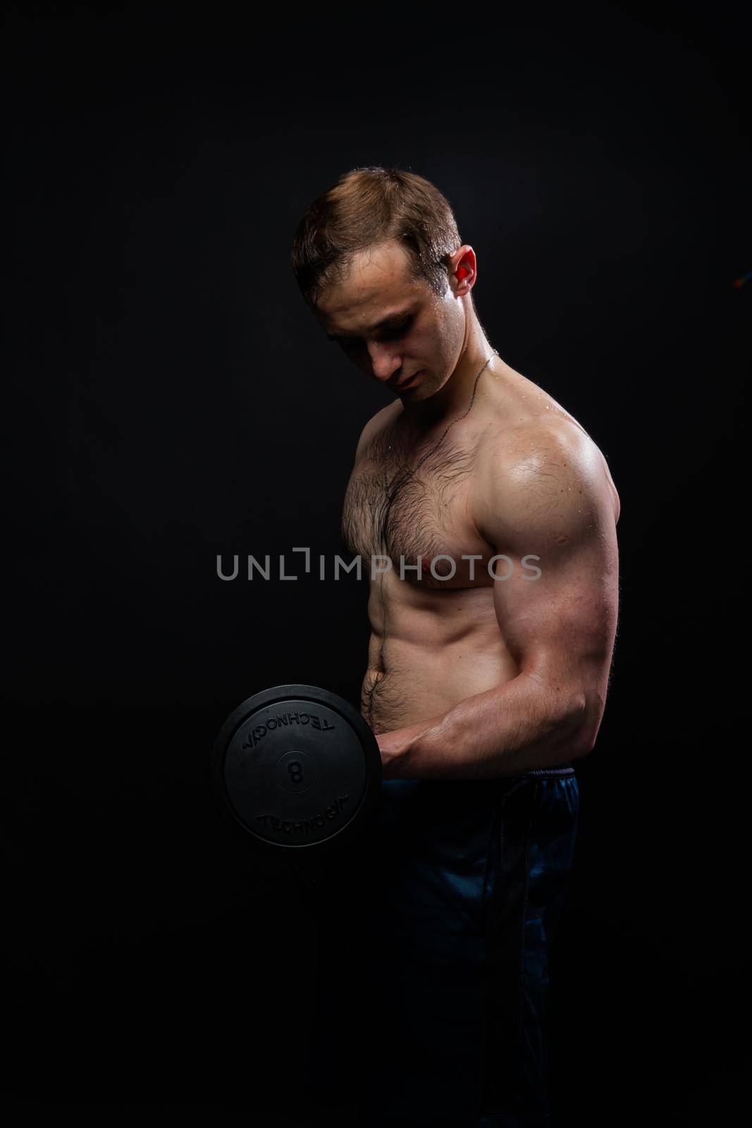 Man on black background keeps dumbbells pumped up in fitness active sexy black, body muscular man bodybuilder powerful, male sportive power, gym fit View from the bottom up good press beautiful muscles hairy chest charisma