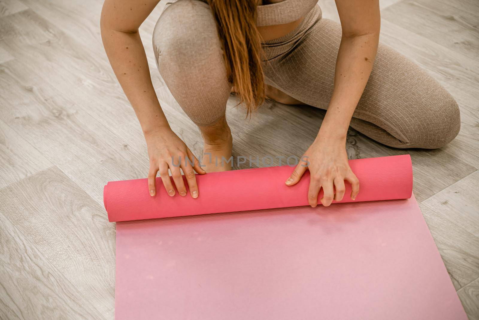 Yoga at home woman rolls pink exercise mat in living room starting to warm up meditation zen well being lifestyle living room apartment